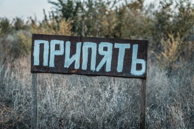 A weathered sign with the word in Cyrillic script, standing in an overgrown, abandoned area, likely referencing the ghost town of Pripyat near Chernobyl. clipart