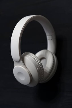 Bir çift beyaz kablosuz kulaklık, yastıklı kulaklıklar ve sol kulaklık üzerindeki kontrol düğmeleri, koyu ahşap bir yüzeye yerleştirilmiş..
