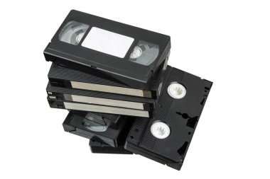 Siyah plastik kutularda bir yığın VHS video kaseti, bazıları etiketli, bir kaset de yan tarafında duruyor.