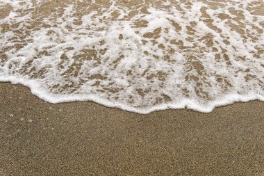 Beyaz deniz köpüğüne yakın çekim Islak, koyu kahverengi kum üzerinde geri çekilen bir dalga.