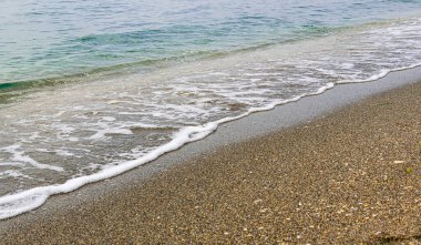 Beyaz deniz köpüğünden ince bir çizgi, berrak turkuaz suyla ıslak bir kumsalda kırılıyor..