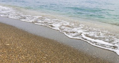 Beyaz deniz köpüğünden ince bir çizgi, berrak turkuaz suyla ıslak bir kumsalda kırılıyor..