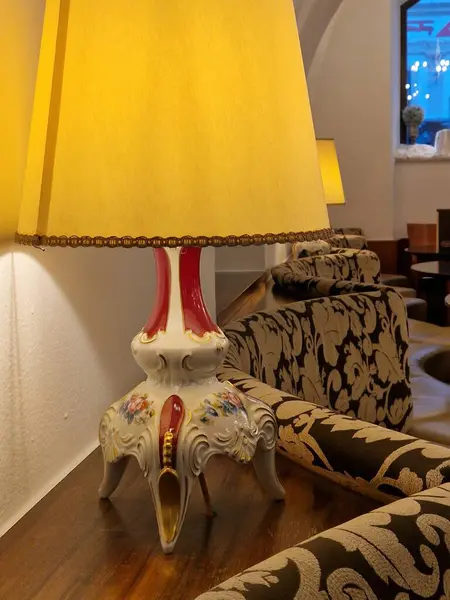 Baroque lamp on a night table next to a sofa spreading dimmed yellow light in the room