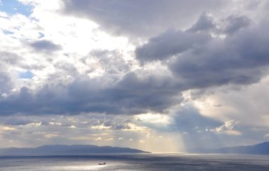 Bulutların arkasındaki güneş, deniz üzerinde parlayan ışık ışınlarıyla. Adriyatik Denizi üzerindeki bulutlara bakan güneş ışınları Hırvatistan 'ın Rijeka kentini dağıttı