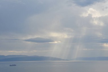 Gökyüzüne Karşı Deniz Manzarası. Güneş ışınları bulutların arasından denize ve bir konteynır gemisine akıyordu. Güneş bulutların arasından Hırvatistan 'ın Rijeka körfezinin sularına doğru yükseldi.