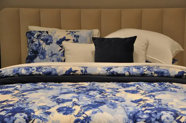 Beautiful beddings with blue and white floral design.Bed with blue floral sheets, white and blue pillows and Soft cushions and blanket.Blue bed furniture with patterned bed linen . Soft satin linen