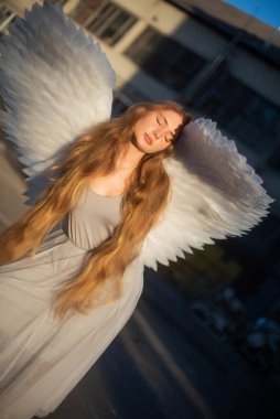 Uzun sarı saçlı güzel bir kız. Büyük kanatlı bir melek kız güneşin önünde duruyor. Kızın üzerine güneş ışınları. Kız güneşin tadını çıkarıyor.