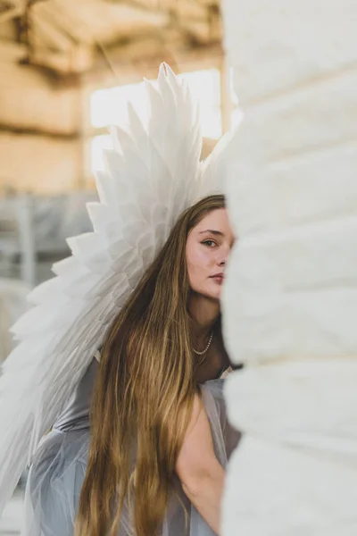 若い美しい天使の女性の肖像画 少女はワークショップに座って壁の後ろから外を見る 背中には大きな白い翼がある 優しい天使 — ストック写真