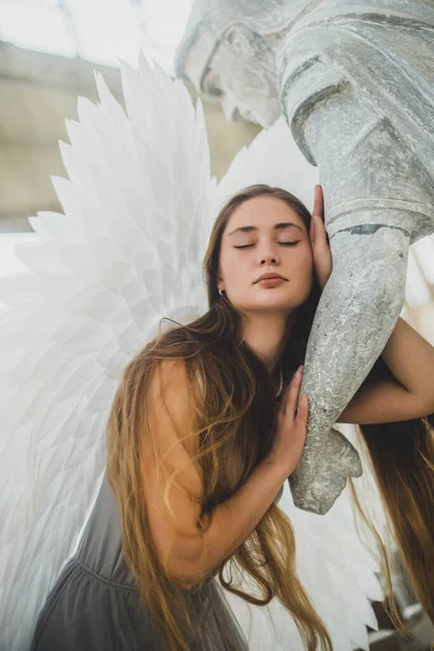 髪の長い天使の女の子と彼女の後ろに大きな白い翼を持つ彼女の手で像を保持している 目を閉じた女の子 — ストック写真
