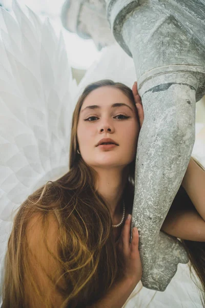 髪の長い天使の女の子と彼女の後ろに大きな白い翼を持つ彼女の手で像を保持している 少女はカメラを覗き込む 肖像画 — ストック写真
