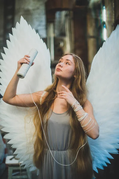 大きな白い翼を持つ天使の女の子 糸の皮でワークショップに立っています 糸は手に巻かれている — ストック写真