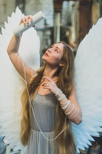 大きな白い翼を持つ天使の女の子 糸の皮でワークショップに立っています 糸が手に巻かれている 女の子は糸を見て — ストック写真
