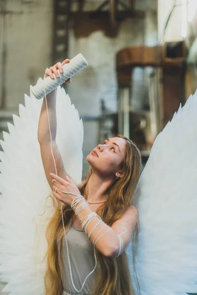 大きな白い翼を持つ天使の女の子 糸の皮でワークショップに立っています 女の子は糸を見て — ストック写真