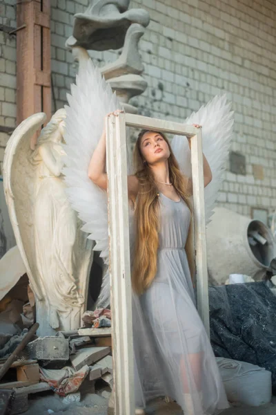 Stock image Architectural heritage. A girl in the image of an angel stands in the workshop against the background of architecture and holds a white frame in her hands