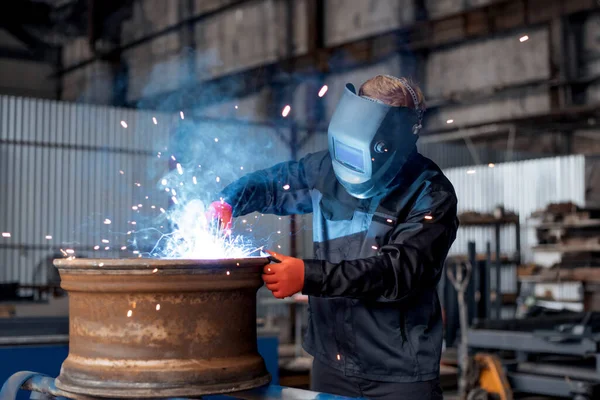 Fabrikadaki çelik yapının elektrik tekerlekleri gıcırdıyor. Metal bir ürünle çalışan bir işçi atölyede kaynak makinesiyle kaynak yapıyor. Endüstriyel üretim. Fabrikada kaynak yapan metal parçası. Turuncu kıvılcımlar. Boşluğu kopyala.