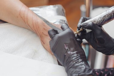 Kuaförde dövmenin kesilip atılmış hali. Dövmeci, dövme makinesinin iğnesini kullanarak cilde mürekkep enjekte ediyor. Stüdyoda çalışan profesyonel bir dövmeci. Seçici odak