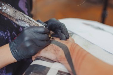 Kuaförde dövmenin kesilip atılmış hali. Dövmeci, dövme makinesinin iğnesini kullanarak cilde mürekkep enjekte ediyor. Stüdyoda çalışan profesyonel bir dövmeci. Seçici odak