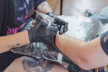 Kuaförde dövmenin kesilip atılmış hali. Dövmeci, dövme makinesinin iğnesini kullanarak cilde mürekkep enjekte ediyor. Stüdyoda çalışan profesyonel bir dövmeci. Seçici odak