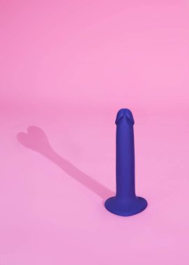 violet dildo sex toys on pink background with a shadow in the form of a heart. Sex toy for adult, dildo vibrator.
