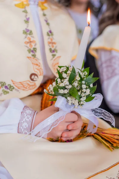 Hands of the First Communion girl holding white flowers and candle. First Holy Communion.