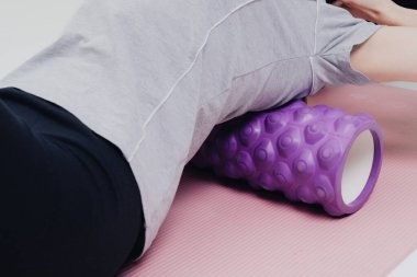 Spor kıyafetli bir kadın, sağlıklı bir yaşam tarzı uyguluyor. Stüdyoda bir masaj rulosuyla hiper hareketli sırt kaslarını miyofasiyal olarak serbest bırakıyor..