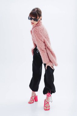 Fotoğraf stüdyosundaki muhteşem modelin tam boy fotoğrafı, şık pembe kürk manto, eşofman altı, güneş gözlüğü, topuklu ayakkabı. Moda, tarz