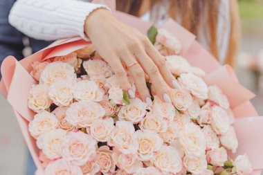 Gelin elini açık pembe bir gül buketinin üzerinde tutuyor. Nişan.