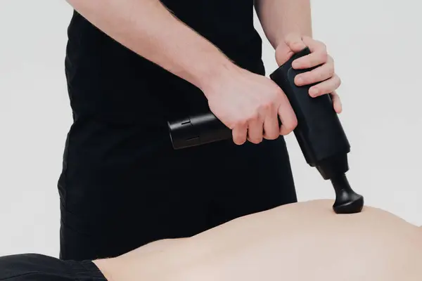 Stock image A therapist using a massage gun on a client's back during a wellness session in a serene treatment room