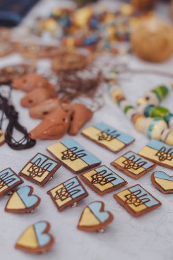 Artisan-crafted ornaments in the form of the Ukrainian coat of arms displayed on a vibrant market table in the afternoon sun. handmade clipart