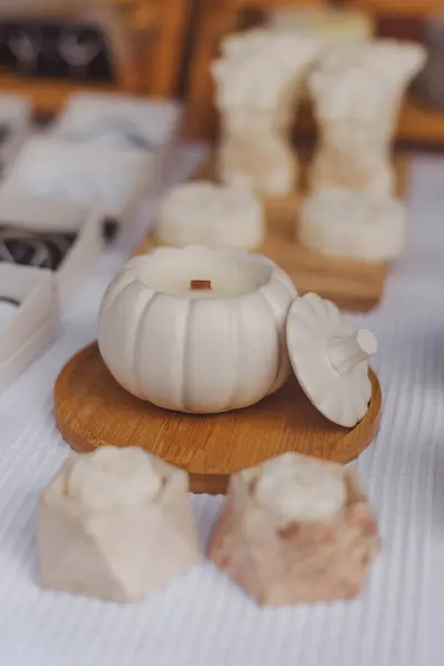 Stock image Handmade ceramic pumpkin candle on a wooden tray with decorative floral molds in a cozy craft market