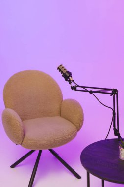 Podcast mikrofonlu rahat sandalye ve masa modern stüdyo ortamında canlı mor bir arkaplan karşısında.
