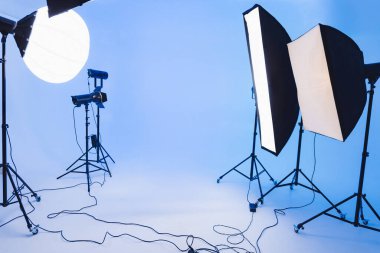 Softbox ve ışıkların mavi bir arkaplan etrafında düzenlendiği iyi organize edilmiş bir fotoğraf seti. Kablolar yere saçılmış, aktif ekipman kullanıldığını gösteriyor..