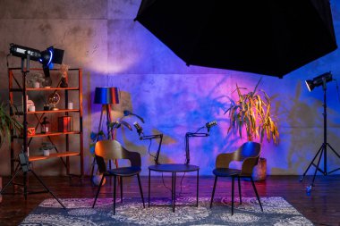 İyi donanımlı bir podcast stüdyosu, canlı ışıklarla aydınlatılmış iki sandalye ve mikrofon sergiliyor. Modern dekor röportaj ve yayınlar için yaratıcı bir zemin sağlıyor..