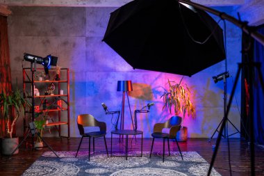 İyi tasarlanmış bir podcast stüdyosu, modern bir mekanda bir mikrofon, üç sandalye ve canlı ışıklandırmanın sergilendiği bir röportaj oturumunu bekliyor. Yaratıcı bir atmosfer yayın deneyimini güçlendirir..