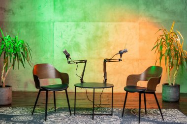 Bu rahat podcast stüdyosu iki ahşap sandalye, kollara monte edilebilir mikrofonlar ve davetkar bir atmosfer yaratan yeşil-turuncu ortam ışıklandırmasıyla röportaj yapmak için tasarlandı..