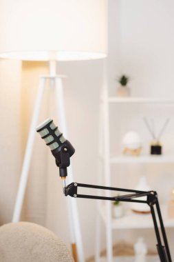 Zarif bir mikrofon, yumuşak ışıklı bir stüdyoda ayarlanabilir bir kola monte edilir. Modern dekor bir lamba ve dekoratif raflar içeriyor. Ses kaydı için hoş bir atmosfer yaratıyor..