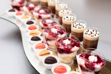 A variety of delightful desserts is arranged on a tray, featuring colorful layered cups, creamy textures, and small baked goods, perfect for a celebration or event. clipart