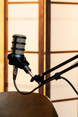 Pürüzsüz, siyah bir mikrofon sağlam bir kürsüye yerleştirildi. Sıcak, davetkar bir podcast stüdyosunda kayıt için hazır. Yumuşak ahşap arka planlar atmosfere eklenir.