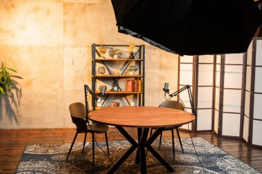 İyi tasarlanmış bir podcast stüdyosunda sandalyeler ve mikrofonlarla çevrili yuvarlak bir ahşap masa yer alır. Yumuşak ışıklandırma davetkar atmosferi arttırır, tartışmaya hazır..