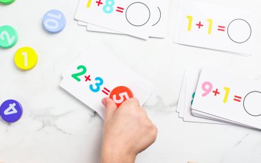 Çocuklar aktif olarak bir matematik aktivitesine katılıyorlar, renkli kartlar ve sayaçlarla denklemleri çözüyorlar, erken eğitimi ve öğrenme ve bağlılığı teşvik ediyorlar..