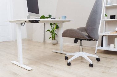 Çağdaş bir merkez ofis, düzgün bir bilgisayar monitörü, ergonomik bir sandalye ve konforlu bir çalışma ortamı sağlayan saksı bitkisi içeren ayakta duran bir masaya sahiptir..