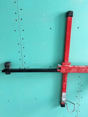 Alçıpan kaldırma aracı, alçıpan panellerinin kurulumu için hazırlıkları gösteren yeşil bir tahtaya güvenli bir şekilde bağlanır. Bu kurulum, ekipmanların bir inşaat sahasında işlevselliğini gösteriyor.