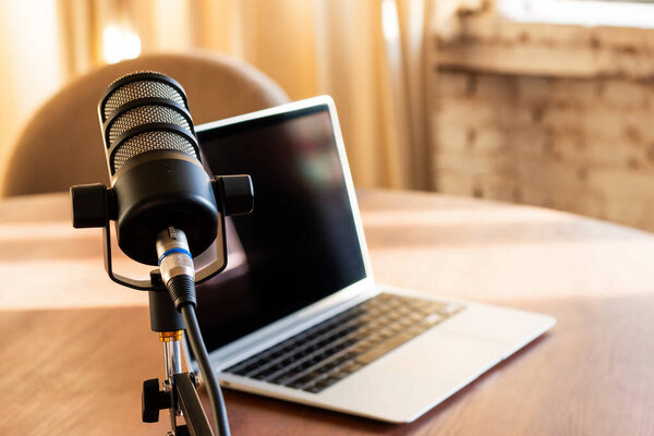 Микрофон расположен на столе рядом с ноутбуком, готовый к живой записи подкаста. Светлая комната обеспечивает четкое звучание и привлекательную атмосферу для обсуждения.