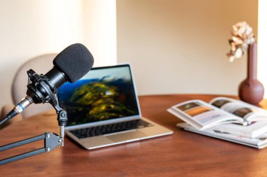 Tahta bir masada dizüstü bilgisayarın yanına yerleştirilmiş bir mikrofon, bir podcast röportajına hazırlık niteliğindedir..