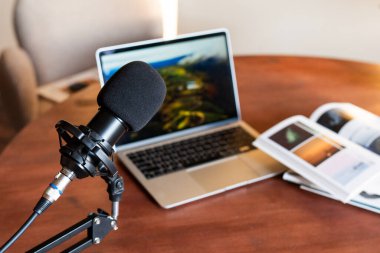 Bir dizüstü bilgisayar eğitimle ilgili görselleri gösterirken, bir mikrofon podcast kaydı için konumlandırılır. Yakınlarda, bir dergide eğitici materyaller yer alır ve eğitime önem verilir.