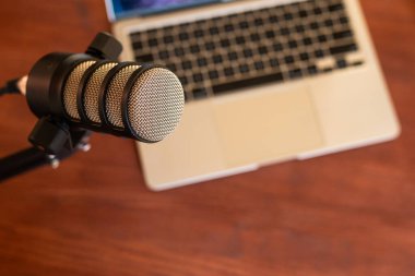 Kürsüye yerleştirilmiş mikrofon açık bir dizüstü bilgisayarın yanında podcast kaydı için hazır. Bu kurulum eğitim ve eğitim mülakatları için idealdir.