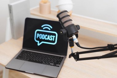 Ayarlar çağdaş bir ofis ortamında ses kaydetmek için yerleştirilmiş bir mikrofon içeriyor. Bir dizüstü bilgisayar bir podcast arayüzü gösterir, mülakatlar ve eğitim içeriği için hazırdır.