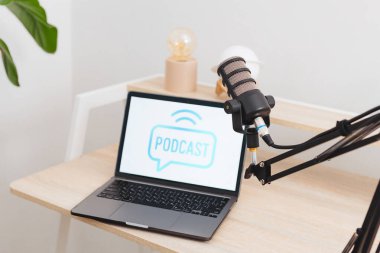 Çağdaş bir ofiste podcast arayüzü gösteren bir dizüstü bilgisayarın yanına bir mikrofon yerleştirilir.
