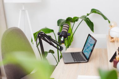 Düzenli bir ofis alanı, bir dizüstü bilgisayarın yanına yerleştirilmiş ayarlanabilir bir kola bağlı bir mikrofon içerir. Bu kurulum, yeşil alanlarla çevrili mülakatlar veya eğitim podcastları için mükemmeldir..