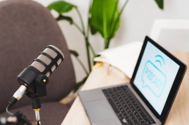 İyi düzenlenmiş bir ofis çalışma alanı, röportaj ve eğitim tartışmaları için ideal olan podcast grafiklerini gösteren bir mikrofon ve dizüstü bilgisayarla donatılmıştır..